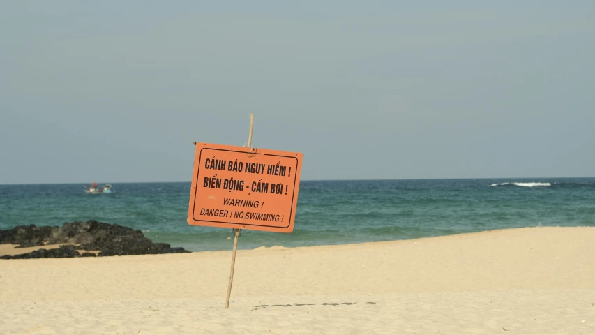 an orange warning sign on beach near ocean