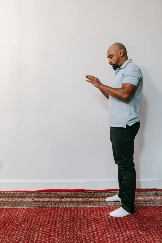 a man stands in front of a white wall in black pants