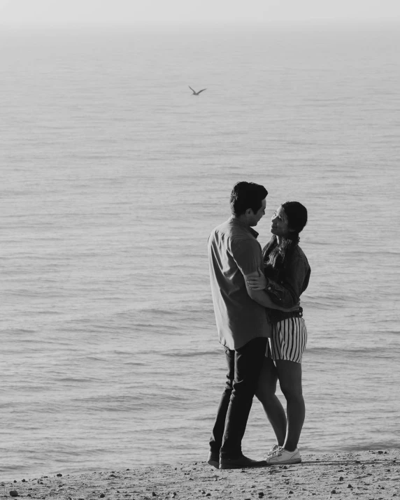 two people stand on a beach as a bird flies overhead