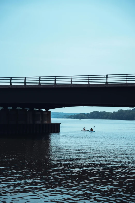 a bridge over the water and two kayakers in the middle of it