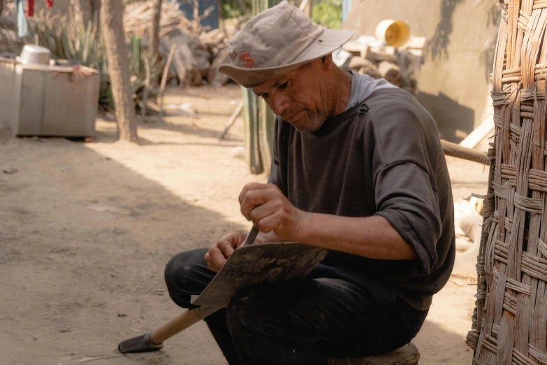 an elderly man sitting and working with hammer in a rural area
