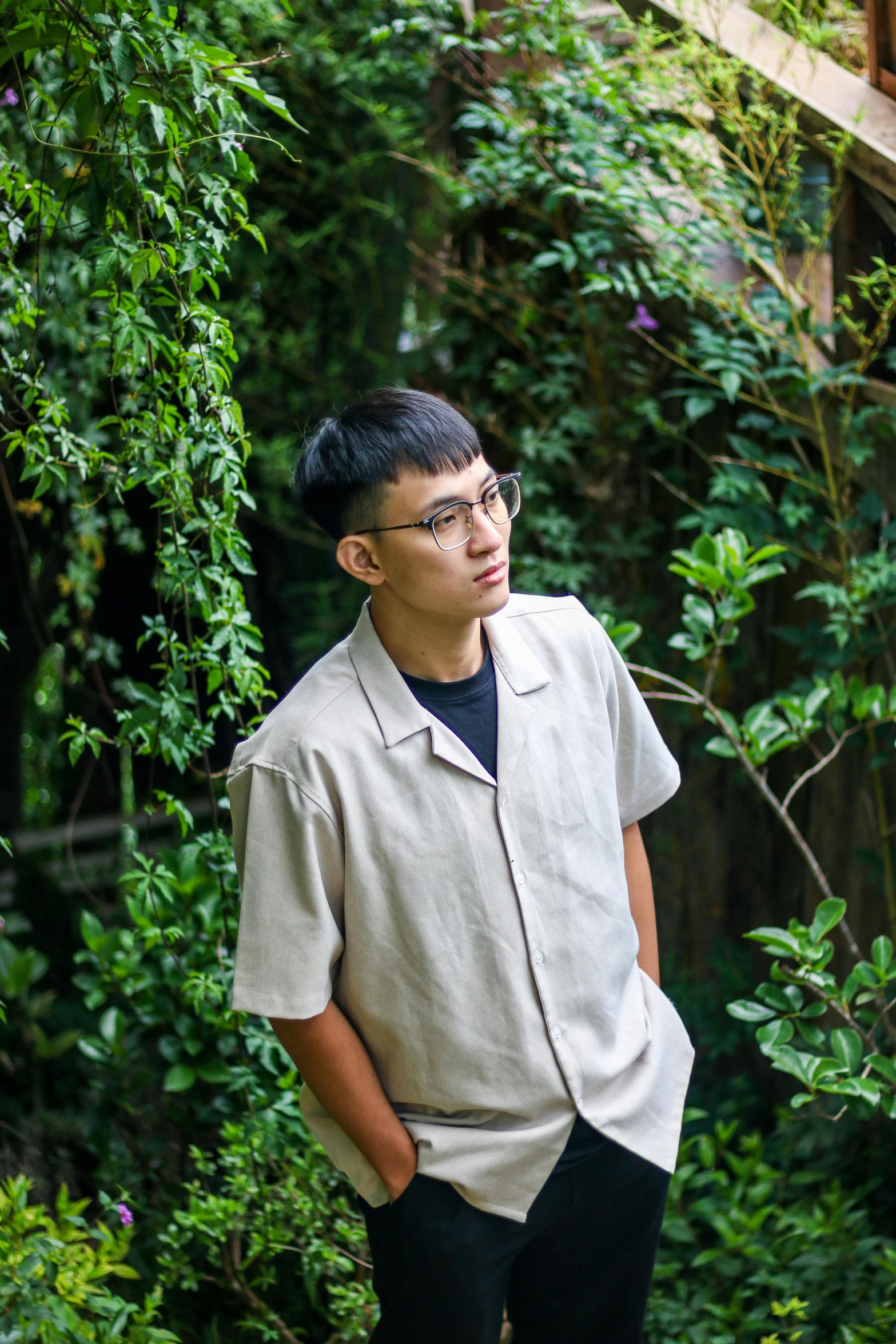 a man with glasses posing outside in front of trees