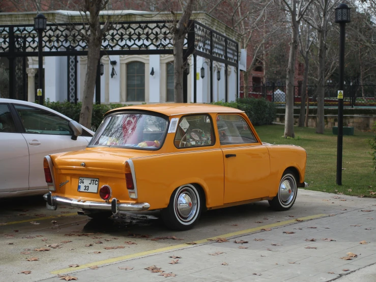 an orange old fashioned car with a white car in the background