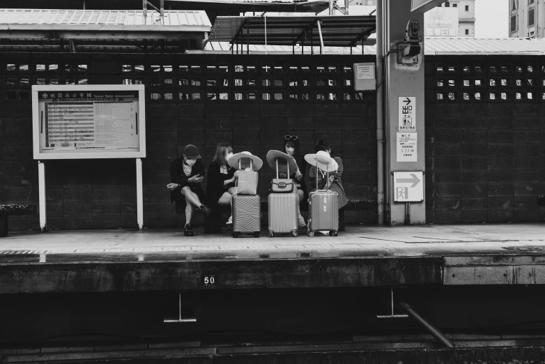 a group of people sit on a bench with luggage at the side of the street