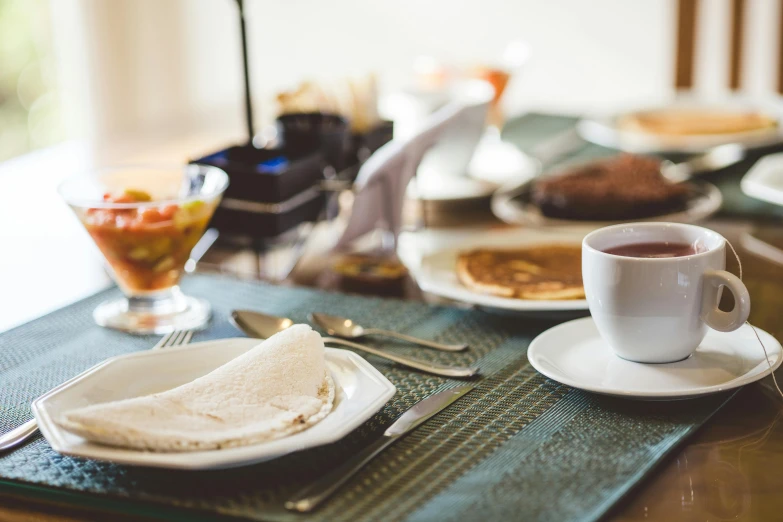 some plates with eggs and muffins, a cup of coffee and a spoon