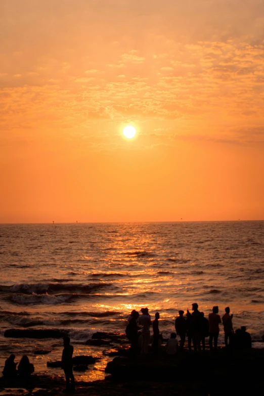 people standing on the shore at sunset watching soing in the distance