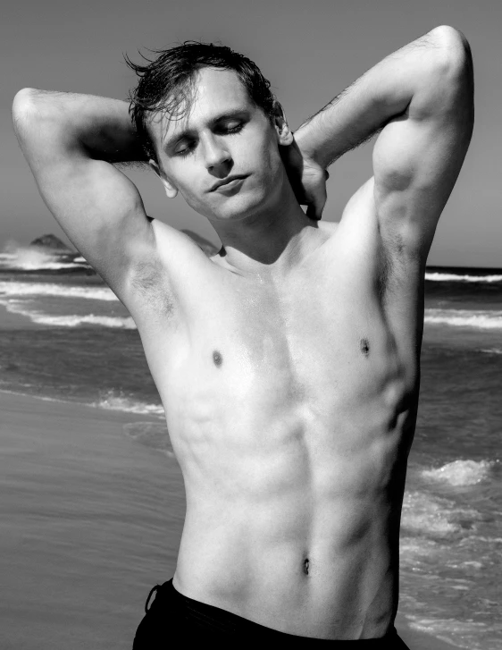 man in bathing trunks posing shirtless on the beach