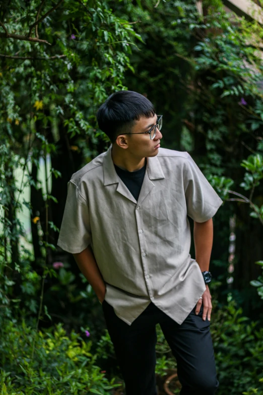 a man wearing glasses and wearing a white shirt standing by trees