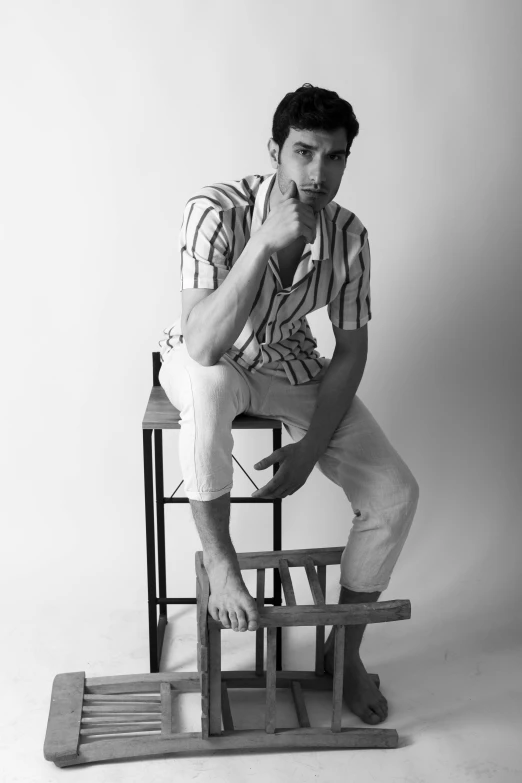 man sitting on wooden stool looking down while holding one hand