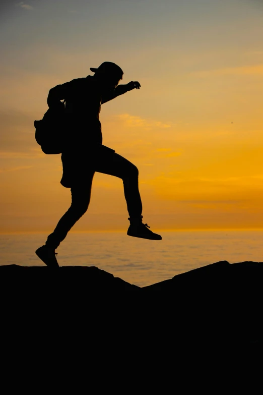 silhouette of man climbing a hill holding backpack