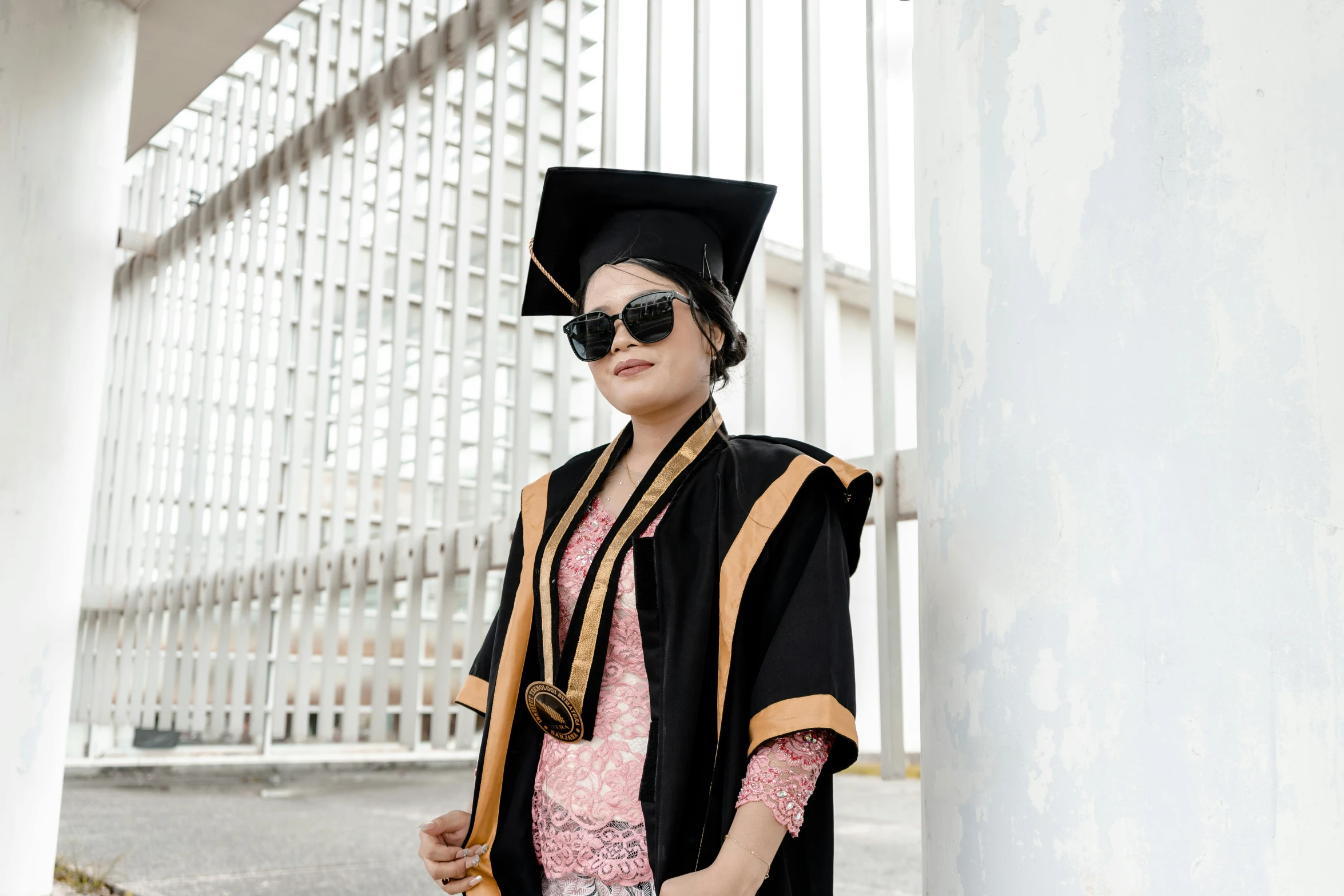 a woman in graduation outfit leans against column