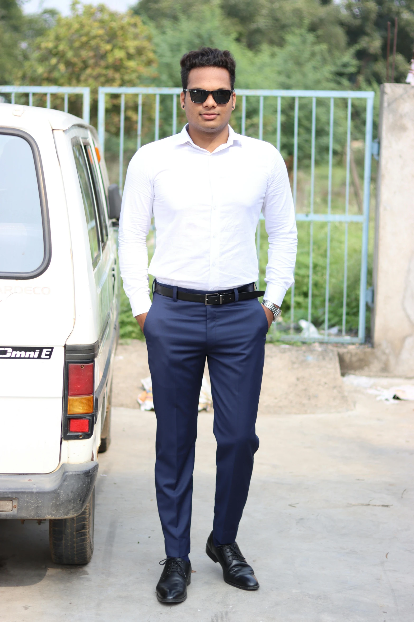 a man with sunglasses stands in front of his car