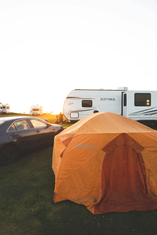 an orange tent is in front of an rv on grass and two cars