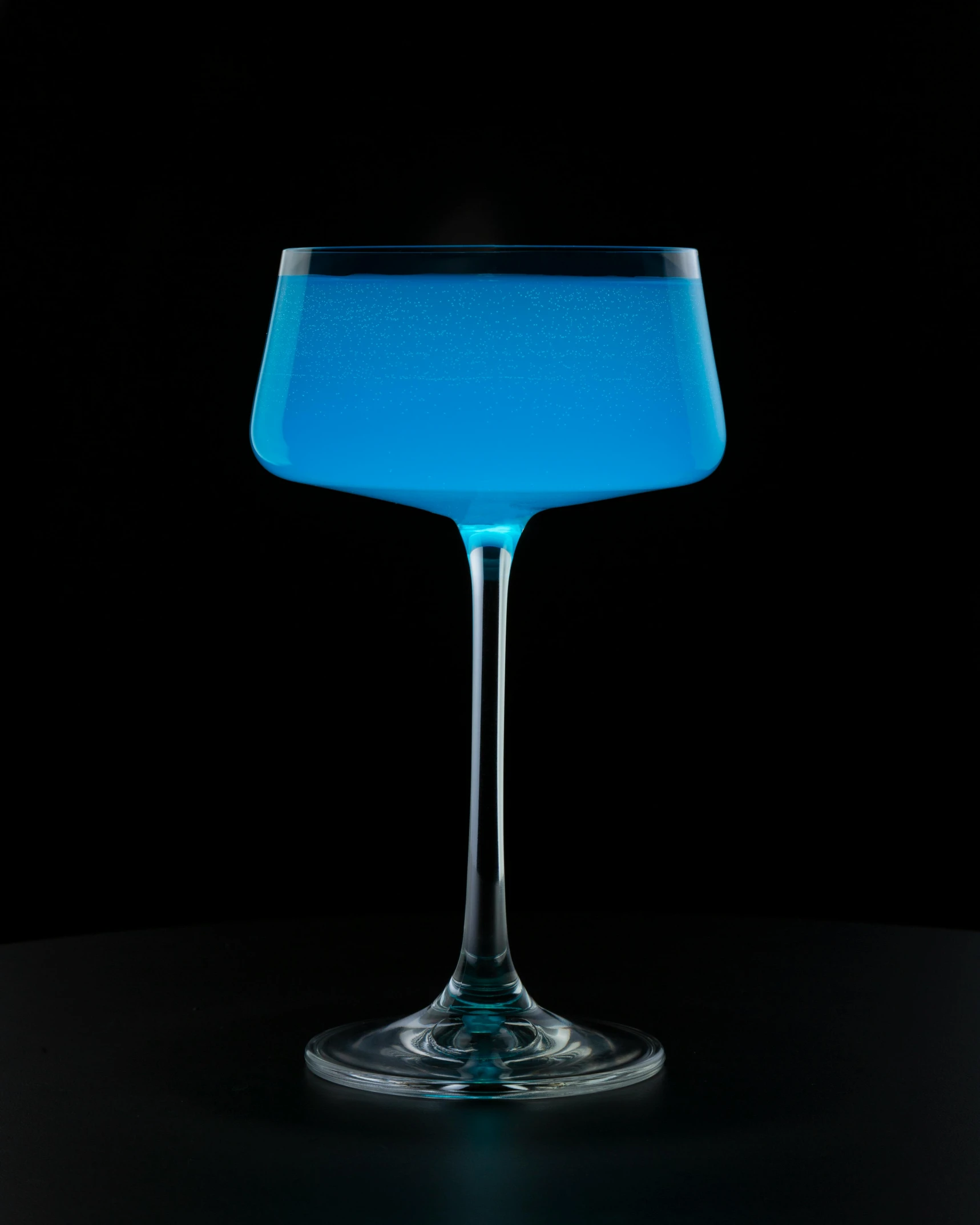 blue liquid in a glass sits on top of a dark surface