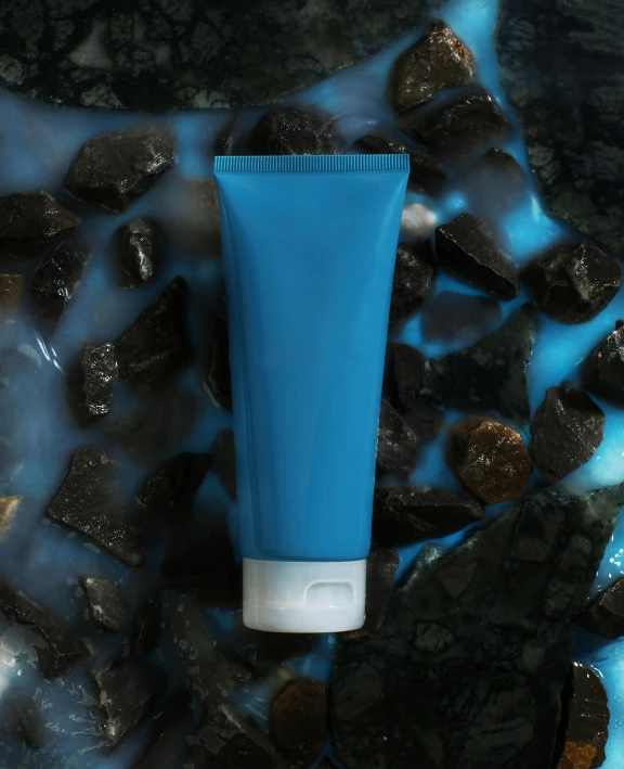 a tube of blue colored hair on a surface with rocks