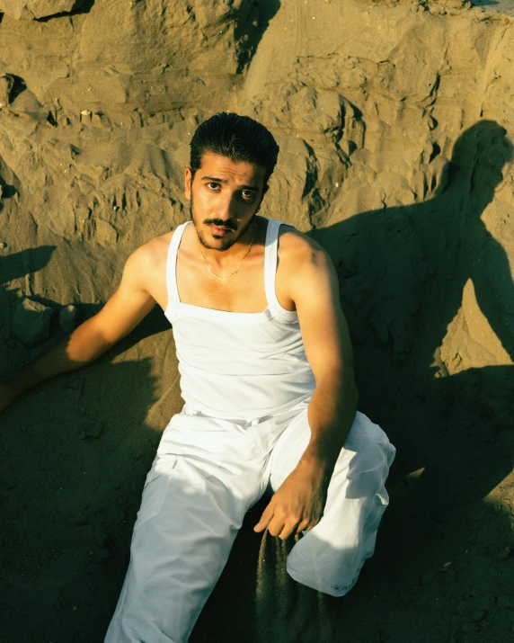 a man sitting down wearing white clothing near rocks