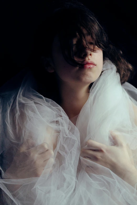 a woman wearing white veils sitting down and holding her hands to her face