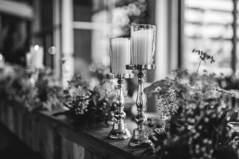 two candles sitting on top of a mantle with flowers in the background