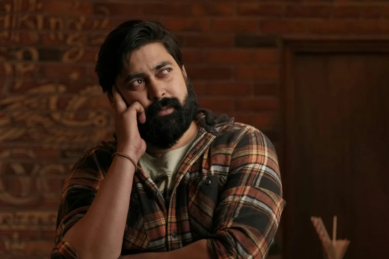 man with black hair, long beard and plaid shirt staring in camera