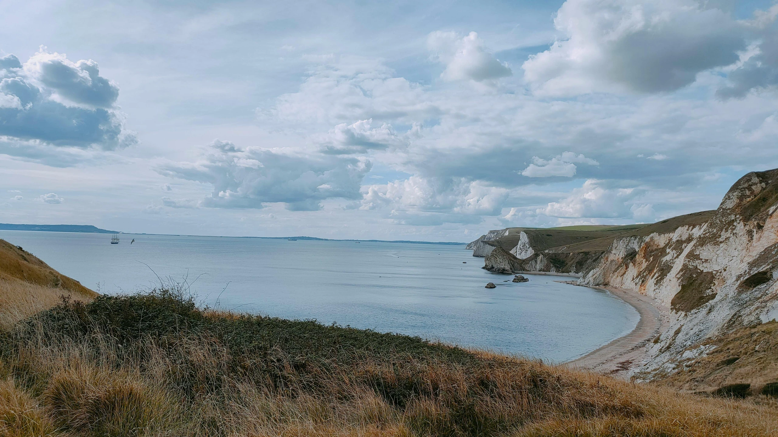 a body of water near a sandy beach and grassy hills