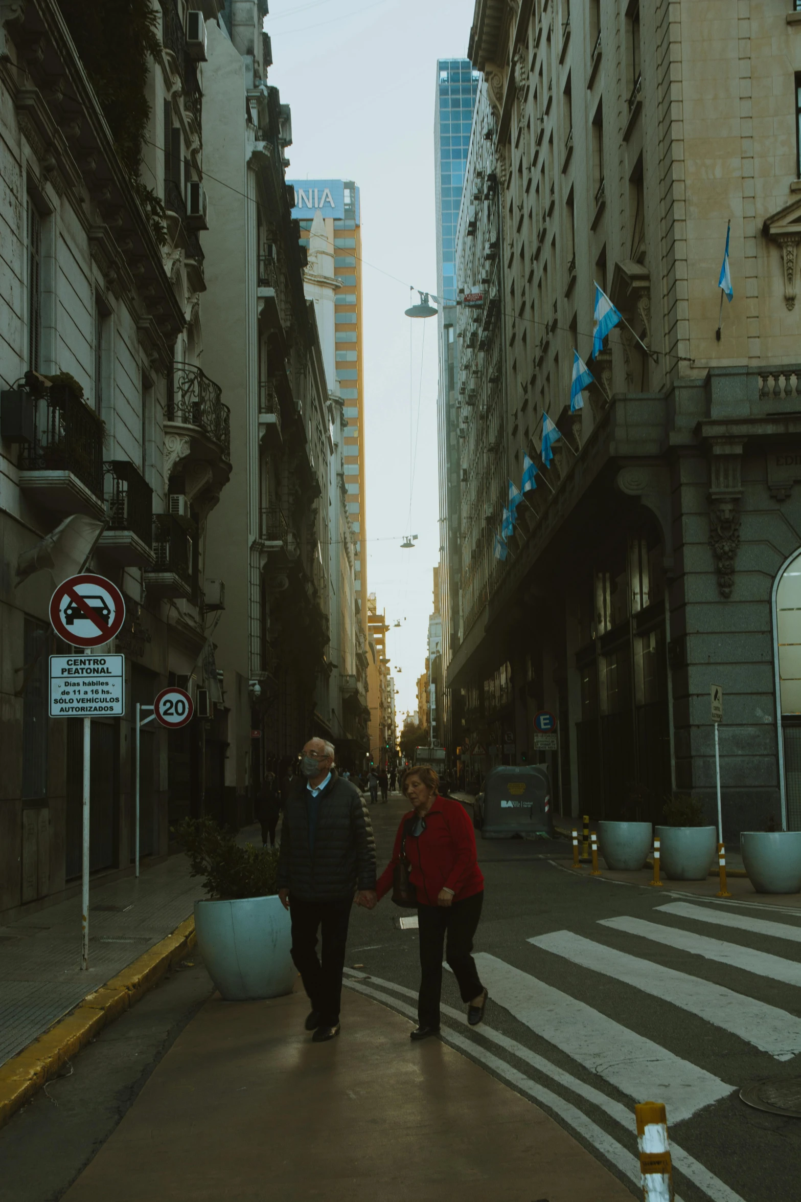 two people crossing a street with tall buildings in the background