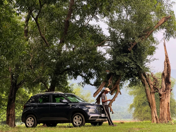 a suv parked by a tree with a person leaning on it