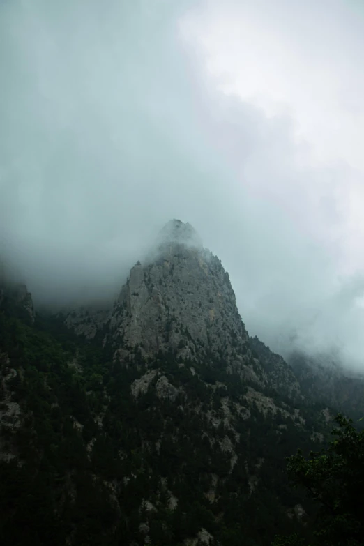 a foggy mountain landscape of clouds, trees and a large stone mountain