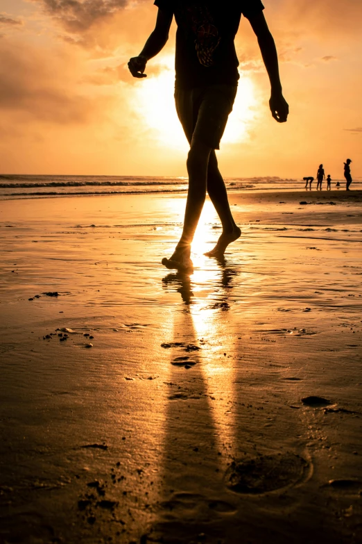 a man walking along the beach at sunset