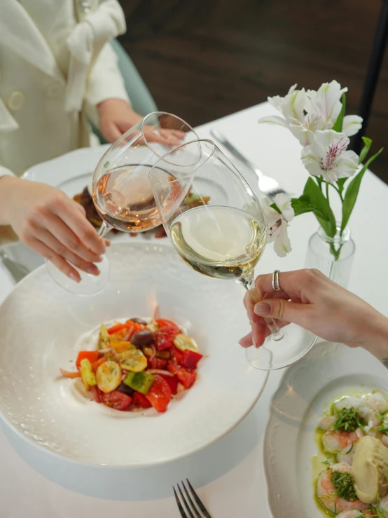 two people toasting wine glasses with salad and fruits on the side