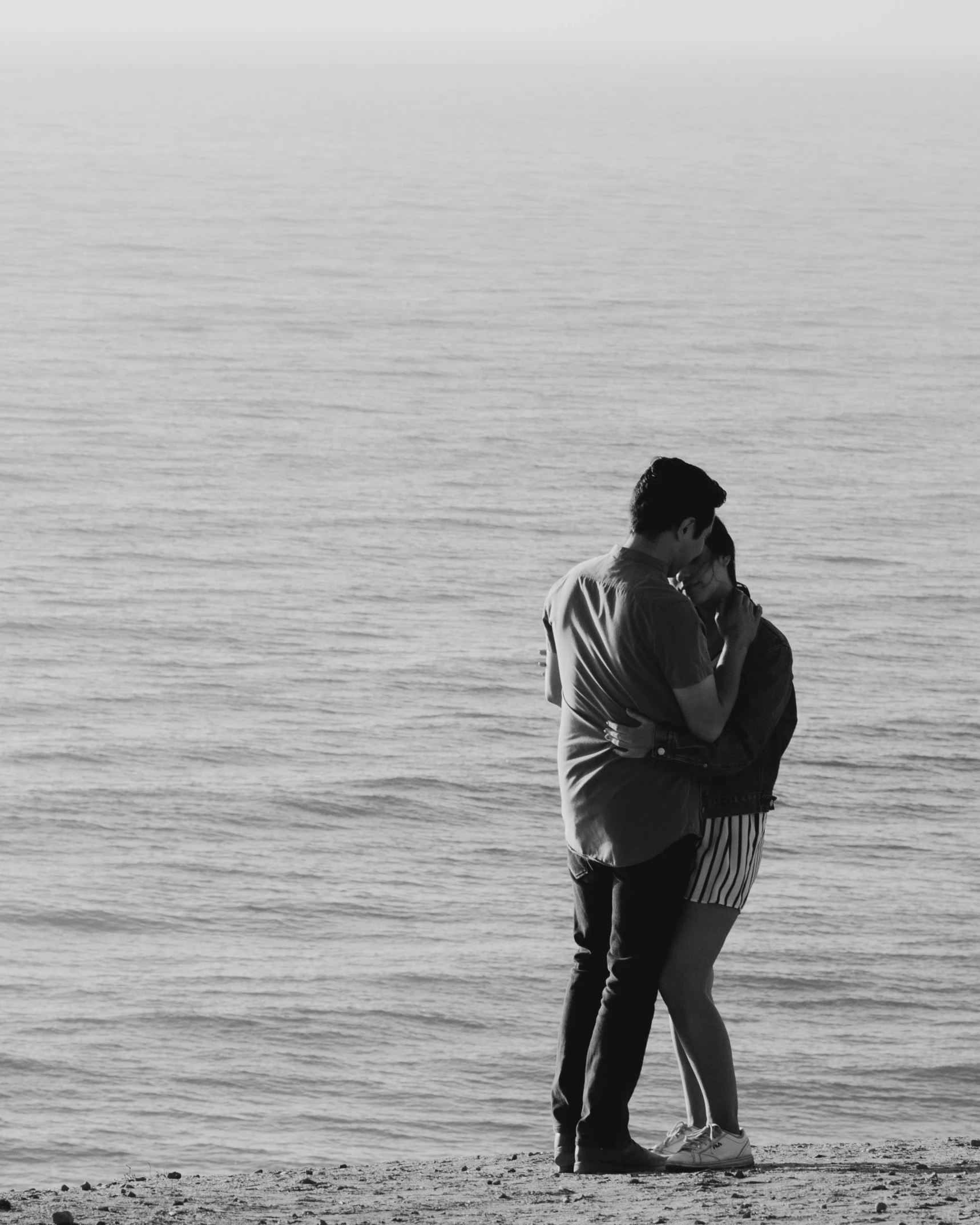 a couple hug as they stand next to the water on the beach