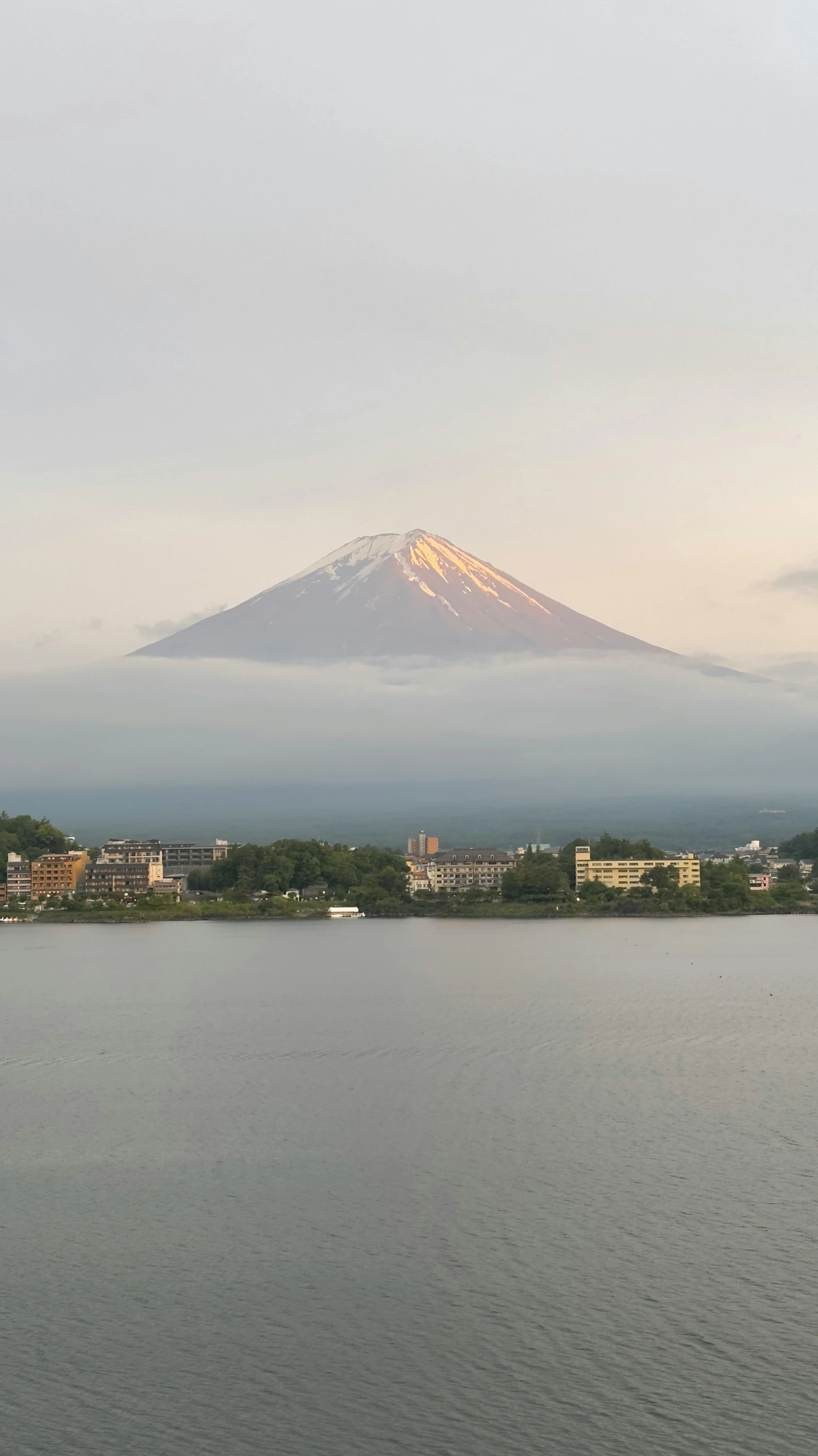 a mountain rises above a lake with buildings in the distance