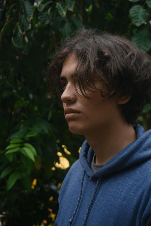 a young man standing in front of a tree looking to the left