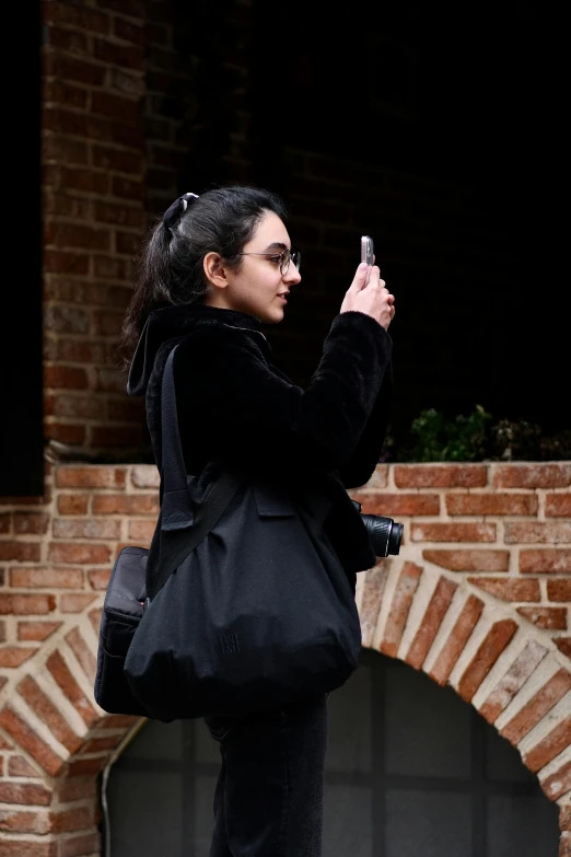 a woman standing next to brick wall holding a cell phone