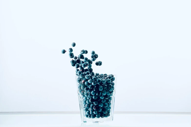 a glass filled with lots of blackberries on a table