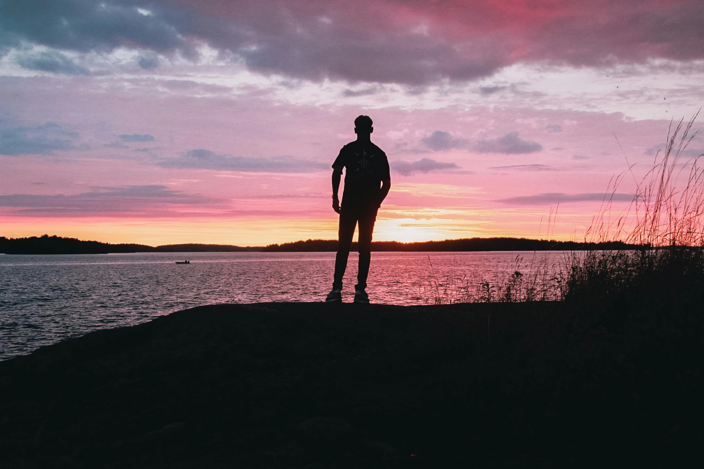 a person stands looking out into the water at sunset