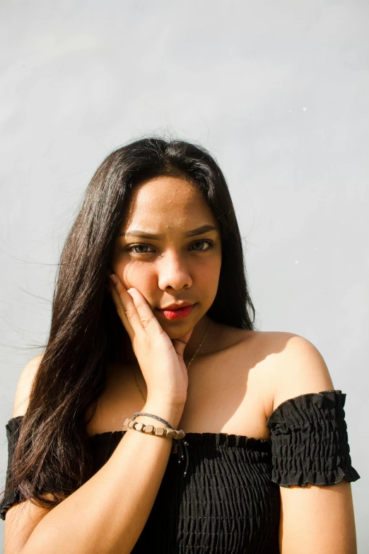 a beautiful woman standing in front of a gray wall wearing a celet