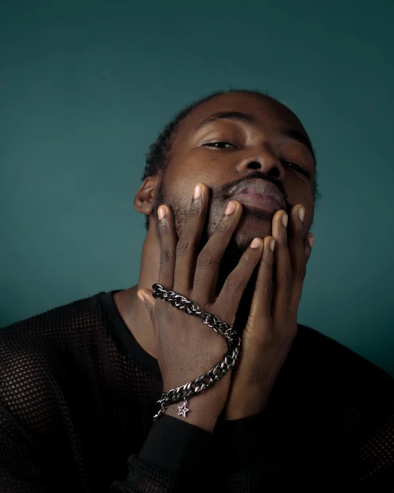 a man with hands together and wearing a chain around his neck