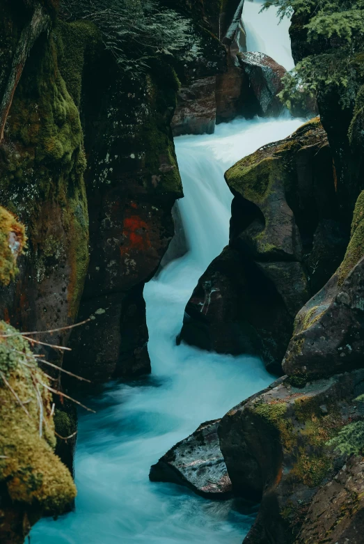 water is running between a large boulders and a tree lined canyon