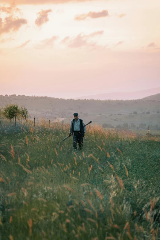 a man stands in an open meadow as the sun sets