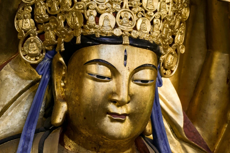 a golden statue of buddha, with a blue ribbon around its head