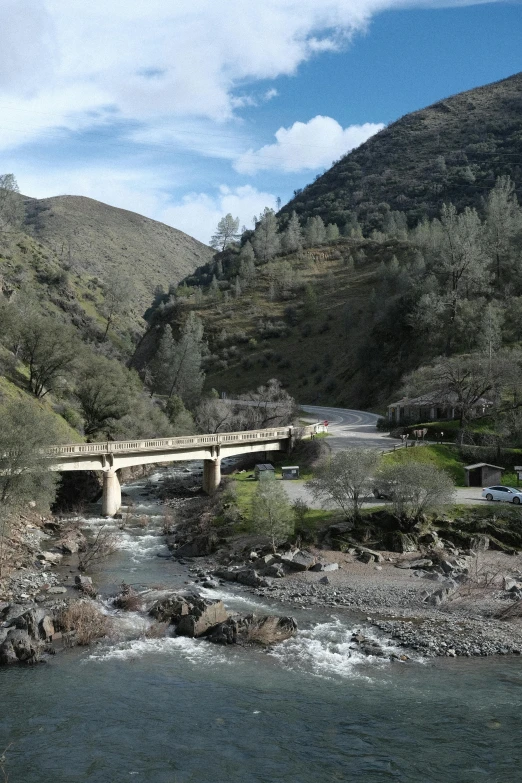 bridge spanning river in a scenic area with mountains and cars