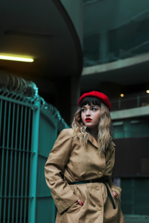 young woman posing in front of a gate wearing a trench coat