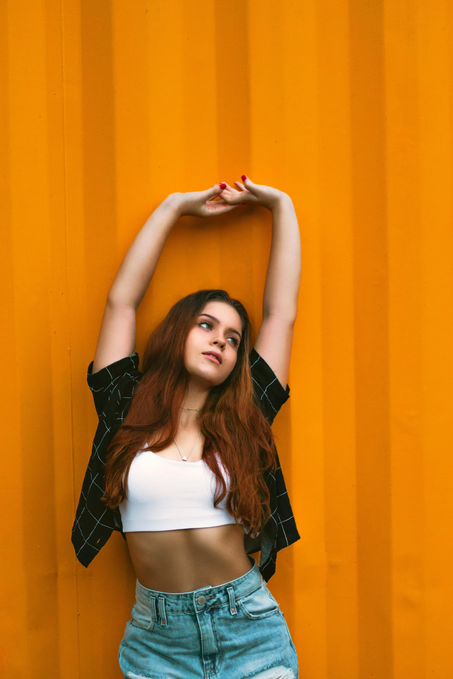 a woman poses with her arms above her head in front of a yellow wall