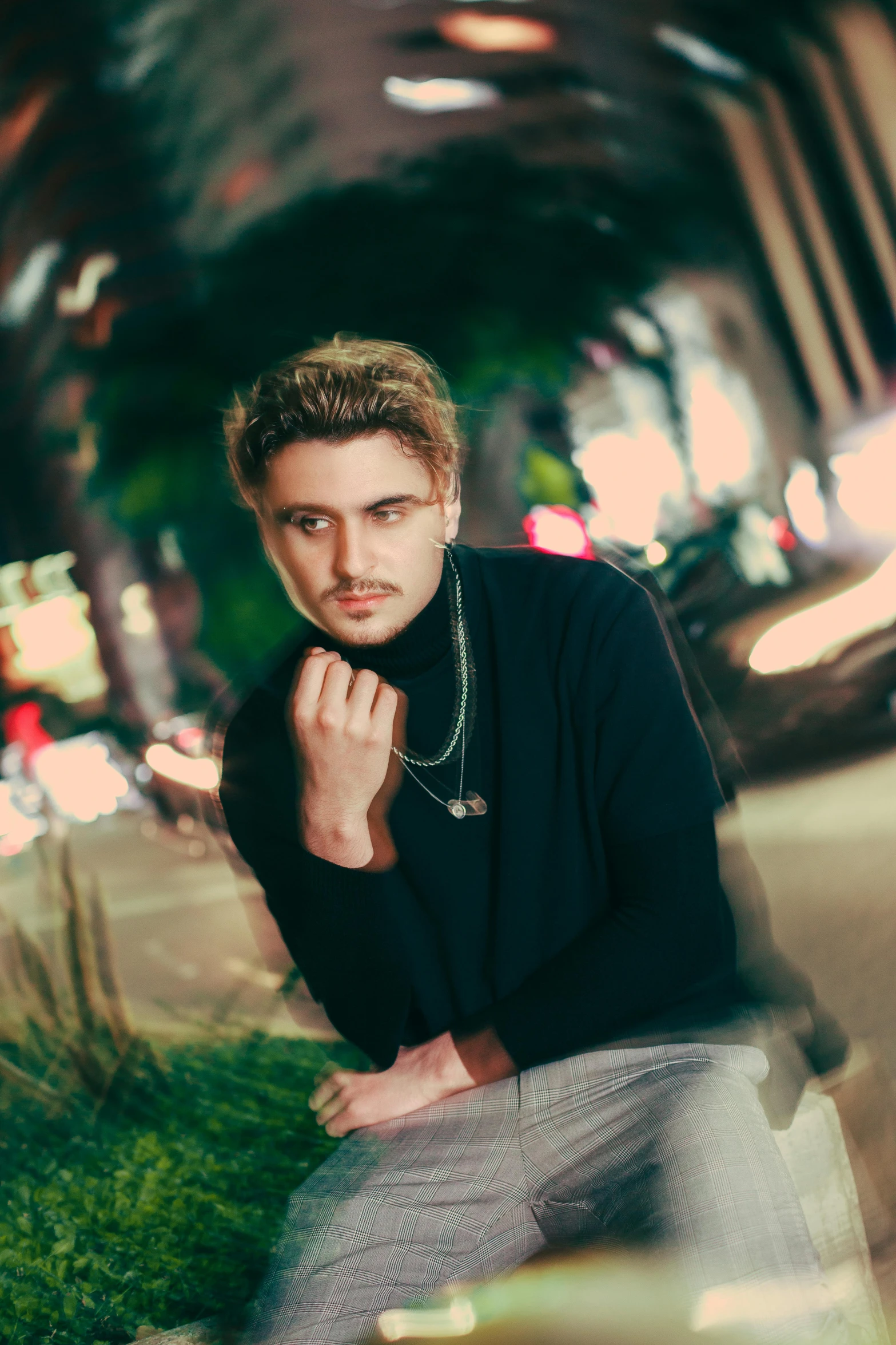 a young man sits on a curb posing for a po