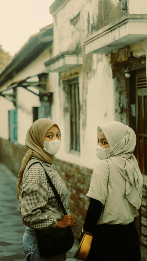 two people with face coverings stand near a building