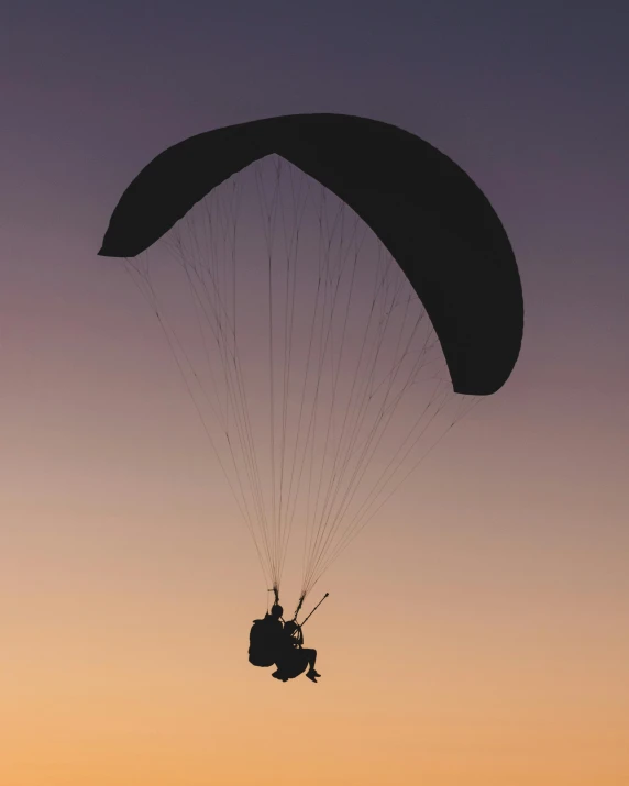 a person is flying over a beach at sunset