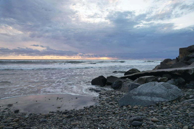 the water is splashing onto the shore under a cloudy sky