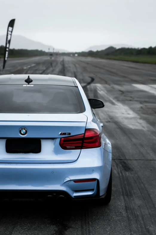 a blue bmw on a wet runway, with hills in the background