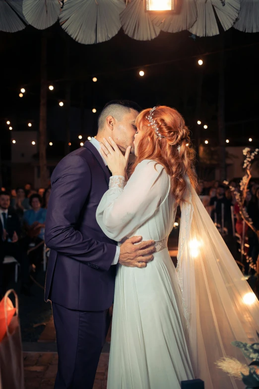 a bride and groom kiss in front of a string of lights