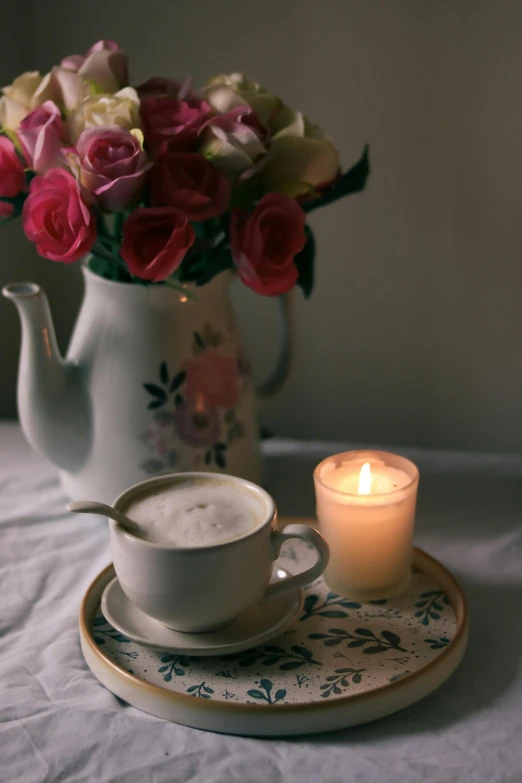 a flower vase with pink and white flowers next to a teacup and candle on a table